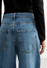 Jeans de mezclilla de color azul claro con una cintura alta, piernas anchas, costuras visibles y dos bolsillos traseros. La tela tiene una textura suave.