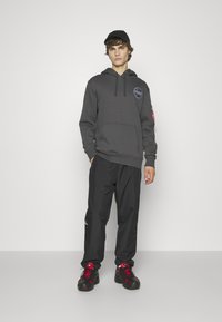 Sudadera con capucha gris con el logo de la NASA, bolso delantero, combinada con pantalones negros y zapatillas negras con acentos rojos.