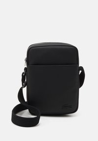Borsa a tracolla nera in nylon strutturato, con chiusura con zip, tasca frontale e tracolla intrecciata. Logo Lacoste impresso in basso.