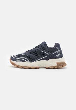 Navy athletic shoes with mesh and suede materials, textured surface, white accents, and a beige rubber sole featuring a patterned tread.