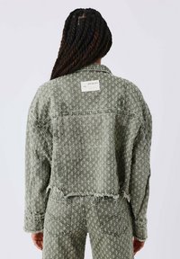 Groene, gestreepte spijkerjacket met een cropped snit, rafelige zoom en bijpassende broek, heeft een merklabel op de achterkant.