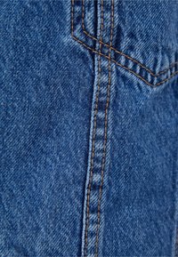 Detailní záběr modré džínoviny ukazující oranžové švy a strukturu podél vertik álního švu a okraje kapsy.