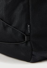 Zaino in rete nera con chiusura a coulisse, superficie texturizzata e una piccola etichetta con il nome del marchio "Snow Peak" in bianco.