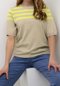 Beige kortærmet sweater med dristige neon gule vandrette striber. Blød tekstur, afslappet pasform. Kombineret med blå denim jeans.