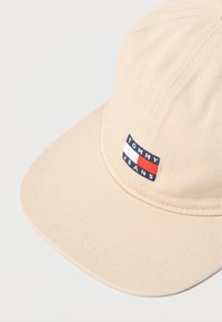 Μπεζ καπέλο με δομημένο σχέδιο, υφασμάτινη υφή και ορθογώνιο ταμπελάκι με το λογότυπο «TOMMY JEANS» σε ναυτικό μπλε, λευκό και κόκκινο.