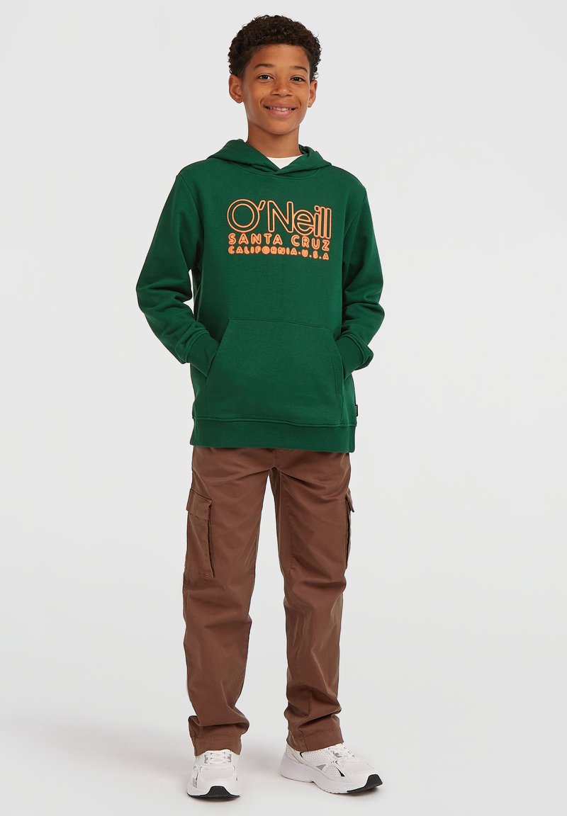 Zelená mikina s kapucí a oranžovým potiskem, kombinovaná s hnědými cargo kalhotami a bílými teniskami. Obsahuje klokaní kapsu a stahovací kapuci.