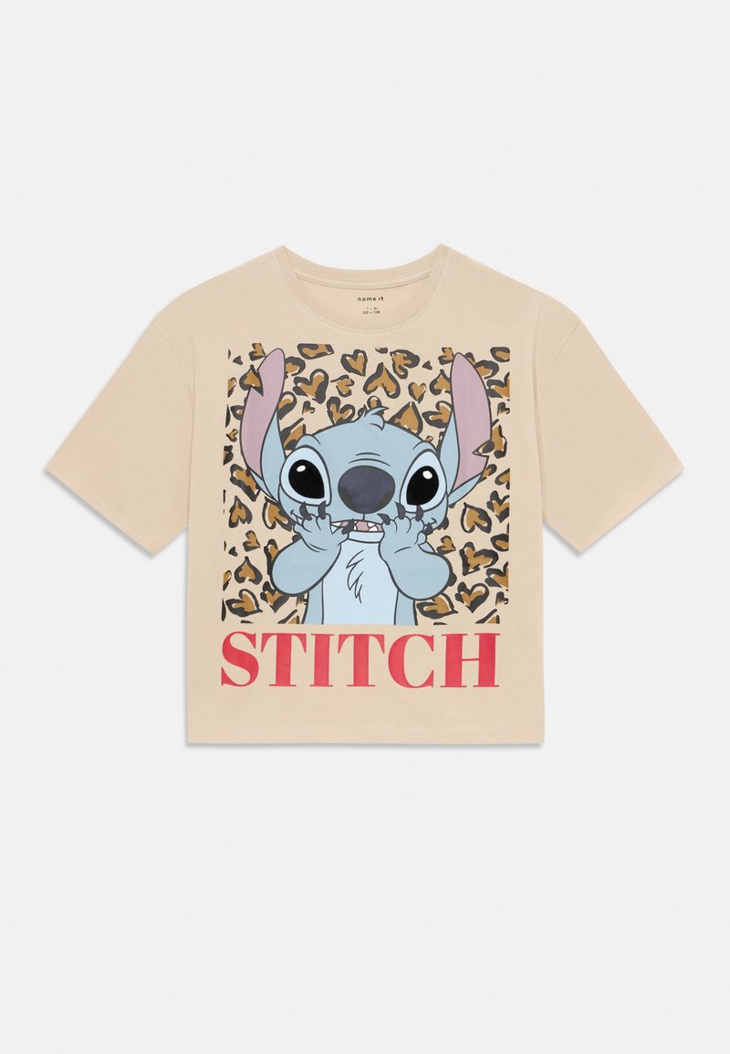 Beidzīgas krāsas T-krekls ar grafiku, kurā attēlots zils multfilmu varonis ar lielām ausīm, ko ieskauj leoparda raksta zīmolējums, un uzraksts "STITCH" sarkanā krāsā.