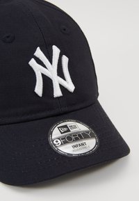 Morska plava sportska kapa od pamuka s bijelim izvezenim NY logotipom, ravnim vizorom i podesivom trakom. Natpis glasi "New Era 9FORTY INFANT."