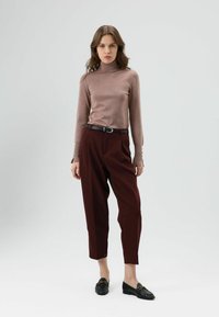 Lichtbruine aansluitende coltrui, bordeauxrode hoge taillebroek met plooien en zwarte loafers met gouden details. Eenvoudige, gelaagde texturen.