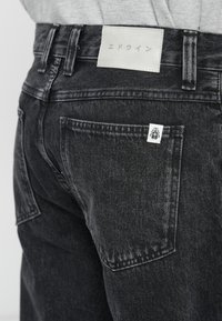 Zwarte denim jeans met een gestructureerde afwerking, voorzien van een leren taillebandlabel en een klein merklogo op de achterzak.