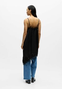 Svart asymmetrisk singlet i lett stoff med blonder. Kombinert med løstsittende blå jeans i denim. Stroppene kan justeres.