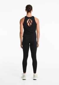 Black athletic tank top with a unique crisscross back design, paired with black leggings and light-colored sneakers. Smooth fabric texture.