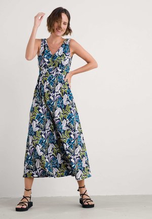 Floral-patterned maxi dress with a blue, green, and purple design. Features a V-neck and a cinched waist, paired with strappy black sandals.