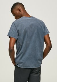 Blue cotton t-shirt with a crew neck and short sleeves, featuring a faded wash and stitched hems. Worn from the back.