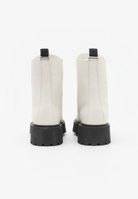 Botines de cuero blanco con una suela texturizada negra, que cuentan con una tira en la parte de atrás y detalles de costura visibles.