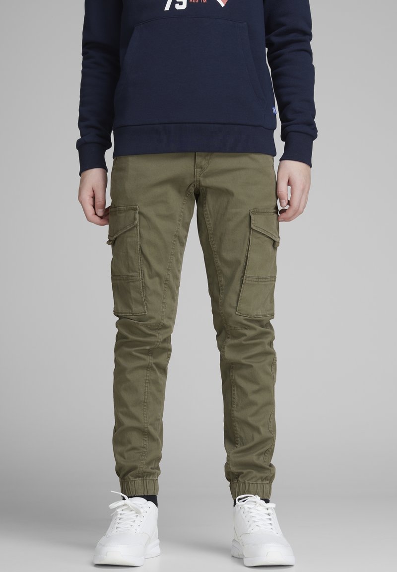 Pantalon cargo vert olive avec plusieurs poches latérales, coupe fuselée et bords élastiques, associé à des baskets blanches et un sweat-shirt bleu marine.