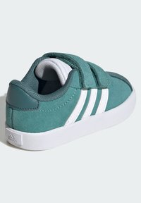 Tyrkysové semišové tenisky s bílými koženými pruhy, nastavitelné suché zipy, polstrovaný límec a zaoblená bílá gumová podrážka.