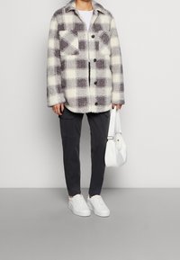 Rutig shacket i krämfärg och grått, tillverkad av fluffigt tyg, med två bröstfickor och svarta knappar. Kombinerad med mörka cargobyxor och vita sneakers.