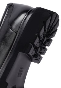 Zwarte leren laars met een glanzend oppervlak en een robuuste zwarte rubberen zool met een diep profiel voor grip.