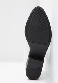 Suela blanca de zapato con forma suave y redondeada; parte inferior de goma negra texturizada para un buen agarre; indicador de tamaño 37 visible en el talón.