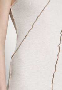 Top de alças texturizado em bege claro com costura em zigzag castanha nas laterais. O tecido tem uma textura suave e um corte ajustado.