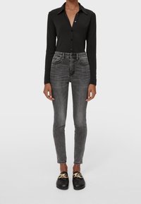 Camisa negra de botones de manga larga, jeans ajustados gris de cintura alta y mocasines negros con detalle de cadena dorada. Texturas suaves de algodón y denim.