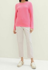 Langärmliger, gerippter rosa Pullover mit rundem Halsauschnitt, kombiniert mit hellen, geraden Hosen und cremefarbenen Slippern.