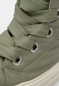 Green, textile high-top sneaker with decorative lacing, metal eyelets, and a white rubber sole. Upper features a smooth, matte finish.