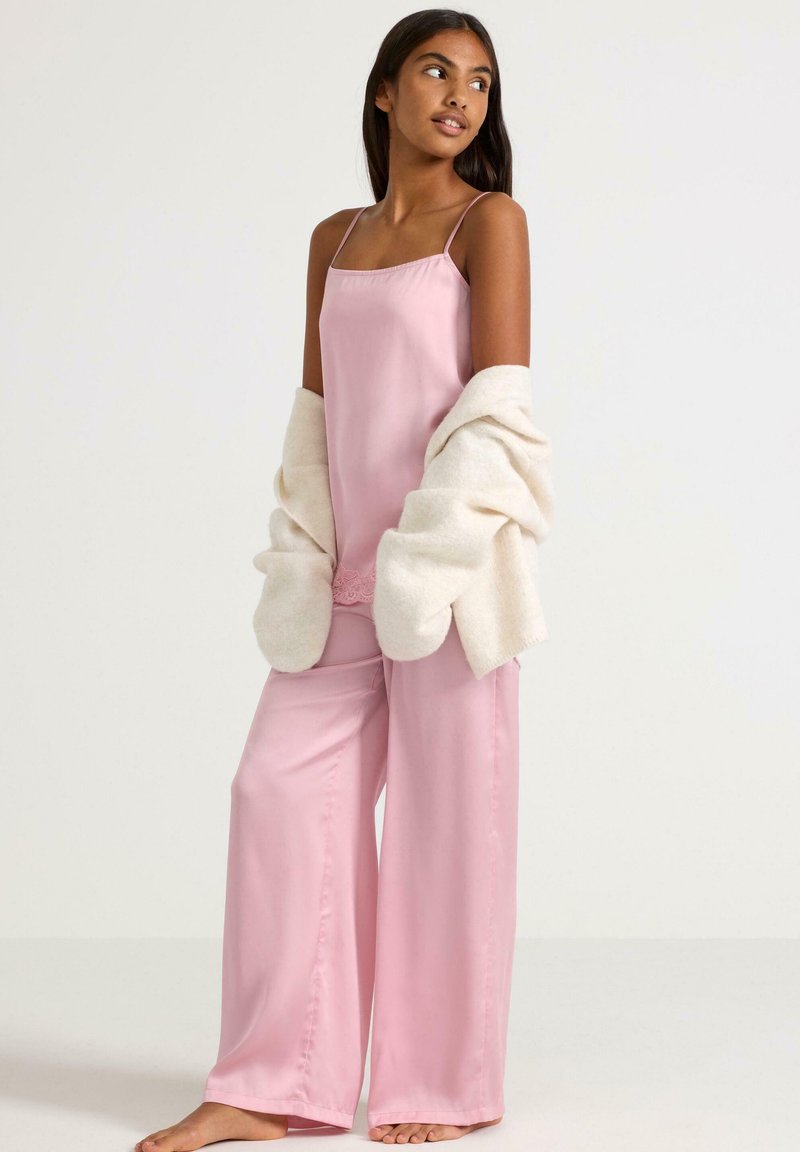 Pajama set in soft pink fabric, featuring a sleeveless top with a lace trim and wide-legged pants. Paired with a cream, fluffy cardigan.