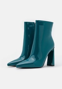 Botines de charol color verde azulado con punta afilada y tacón grueso, que cuentan con un cierre de cremallera lateral y un acabado brillante y suave.