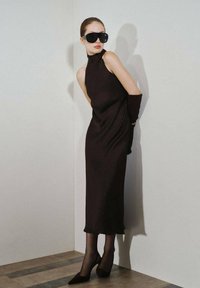 Un vestido negro sin mangas con un cuello alto, combinado con medias negras transparentes y tacones de punta. Unas grandes gafas de sol negras completan el look.