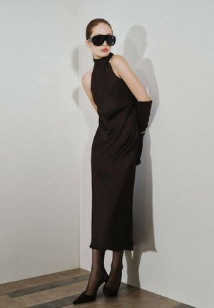 Un vestido negro sin mangas con un cuello alto, combinado con medias negras transparentes y tacones de punta. Unas grandes gafas de sol negras completan el look.