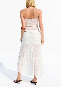 Strapless white lace dress with a textured pattern, featuring a fitted top and flared skirt. Worn with black heeled sandals.