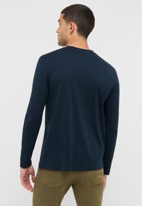 Hosszú ujjú, sötétkék póló, puha pamutból készült, kerek nyakkivágással és minimális dizájnnal, látható minták vagy díszítések nélkül.