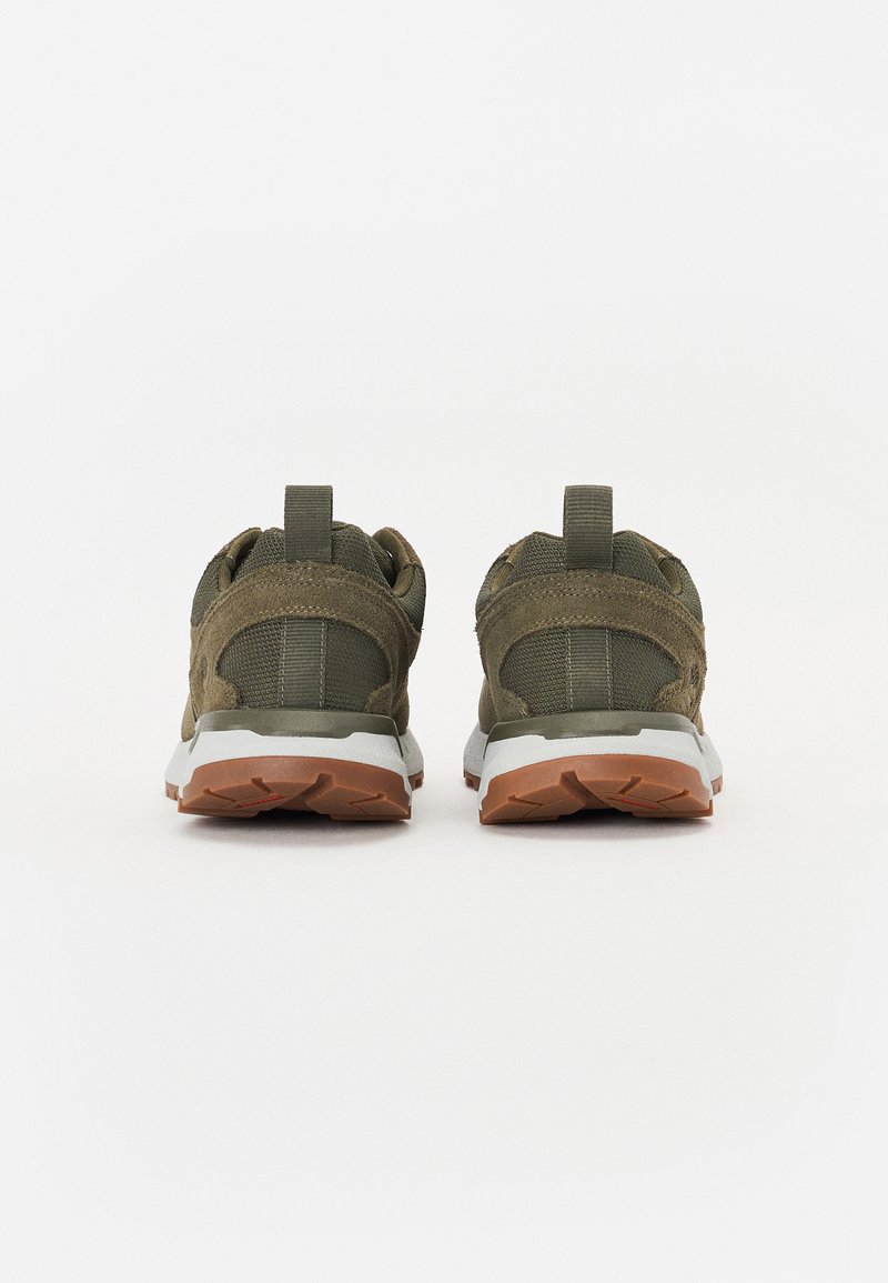 Zapatillas deportivas de color verde oliva con parte superior de malla y gamuza, suela de goma, lengüeta en el talón y media suela blanca con patrón de tracción marrón.