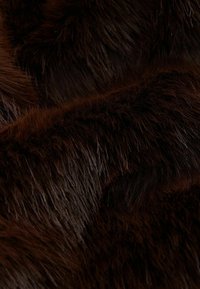 Tissu en fausse fourrure marron foncé avec une texture épaisse et douce, présentant des longueurs de fibres variées créant une apparence douce et superposée.