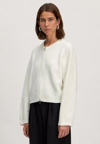 Witte geribbelde zip-up trui, cropped ontwerp, ronde halslijn, verlaagde schouders en textuurstof. Gecombineerd met een zwarte onderkant.