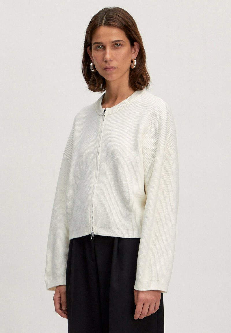 Witte geribbelde zip-up trui, cropped ontwerp, ronde halslijn, verlaagde schouders en textuurstof. Gecombineerd met een zwarte onderkant.