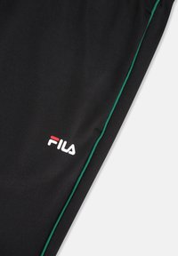 Czarny materiał z zielonym obszyciem i logo FILA w kolorze białym i czerwonym na dolnej części ubrania, prawdopodobnie nogawce spodni.