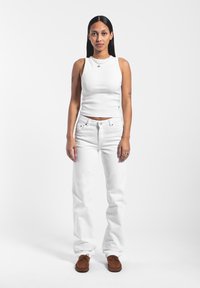 Top blanco de canalé combinado con jeans rectos blancos y zapatos mocasín marrones. El conjunto presenta un diseño minimalista y una silueta ajustada.