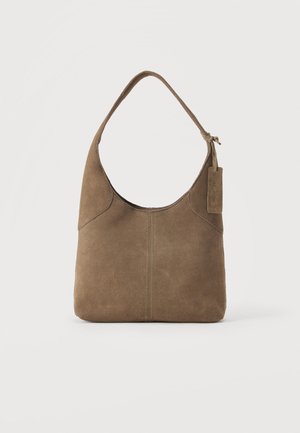 Sac à bandoulière en daim marron avec une large sangle et une petite étiquette en cuir suspendue près de la poignée sur un fond uni.