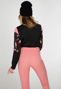 Haut à manches longues avec corps noir et manches à motifs roses et noirs ; associé à un pantalon taille haute rose. Bonnet en laine noir.