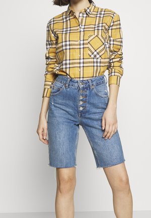 Yellow plaid button-up shirt with long sleeves, paired with high-waisted blue denim shorts featuring a five-button front and frayed hem.