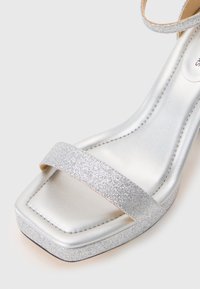 Silberne Sandale mit quadratischer Spitze, glitzerndem Riemen, metallischem Finish und strukturiertem Blockabsatz für zusätzlichen Halt und Stil.