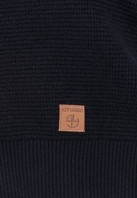 Marineblauer Strickpullover mit strukturiertem Körper und geripptem Saum. Mit einem quadratischen Lederlabel mit dem eingeprägten Schriftzug "KEY LARGO".
