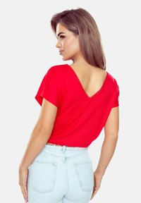 Czerwona koszulka z krótkim rękawem i dekoltem w serek, z fakturowanym wykończeniem. Połączona z jasnoniebieskimi dżinsami o wysokim stanie. Gładki materiał.