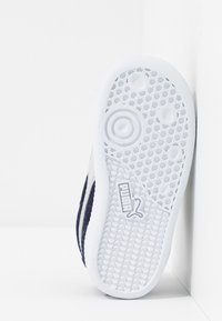 Vit sneaker sula med texturerad gummi, med cirkulära mönster och en logotyp. Ovandelen har en marinblå tyg och vita accenter längs sidorna.