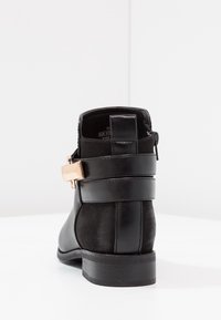 Černé kotníkové boty s hladkou koženou svrchní částí, texturovaným zadním dílem, kovovým sponovým akcentem a nízkým vrstveným podpatkem. Obsahují boční zip.
