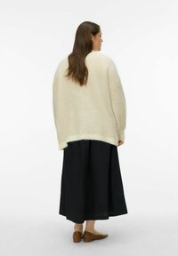 Liels krēmkrāsas džemperis ar struktūrētu adījumu, pārklāts virs melnas svārku, kombinēts ar brūnām dzīvoklēm. Vienkāršs dizains un nomierinošas krāsas.