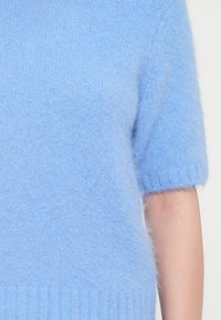 Maglione corto azzurro con maniche corte, realizzato in un materiale morbido e goffrato, con orlo a coste e una vestibilità rilassata.